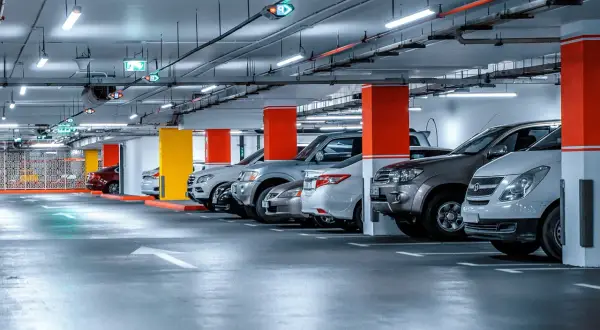 Jasne, oto opis alternatywny:

Rząd samochodów zaparkowanych pod jasnym oświetleniem parkingu. Kolorowe słupy i strzałki kierunkowe wskazują drogę.