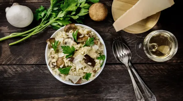 Risotto ai funghi cremoso, guarnito con prezzemolo fresco e scaglie di parmigiano. Un bicchiere di vino bianco completa questo perfetto abbinamento vino funghi.