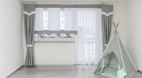 Jak dobrac firanki do okna? Szare zasłony w gwiazdki i białe firanki tworzą przytulną atmosferę. Obok namiot tipi.