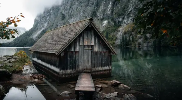 Alte Holzhütte am Ufer des Obersee-Sees, umgeben von steilen Felswänden und nebliger Atmosphäre.