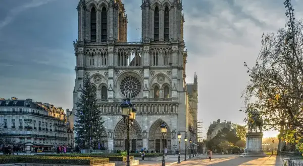 La maestosa cattedrale di Notre Dame de Paris, con le sue torri imponenti e un albero di Natale illuminato, si erge maestosa sotto un cielo nuvoloso.