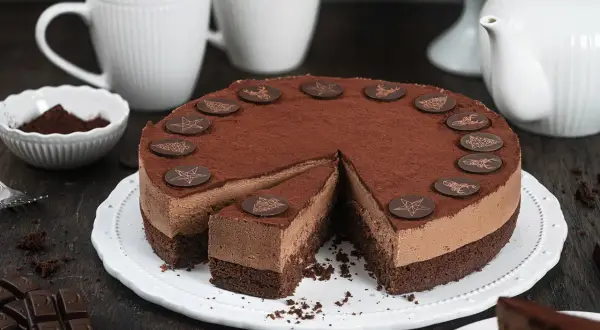 Schokocreme Torte mit Mascarpone, dekoriert mit Schokoladen-Emblemen. Ein Stück ist bereits angeschnitten.