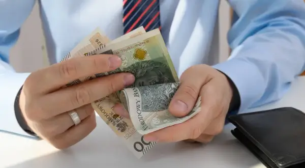 Mężczyzna w koszuli i krawacie liczy polskie banknoty. To mogą być koszty pracodawcy związane z wynagrodzeniem.