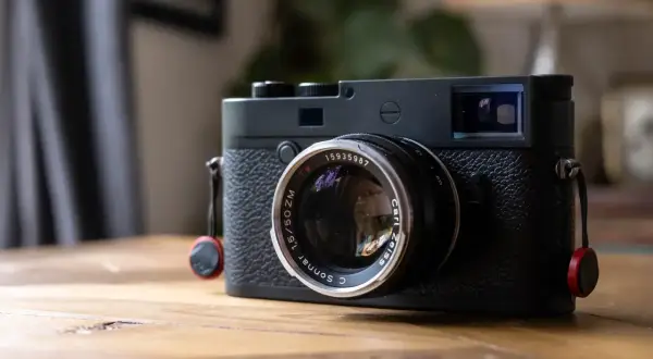 A black Leica M10P camera with a Carl Zeiss Sonnar lens sits on a wooden table, ready to capture life's moments.