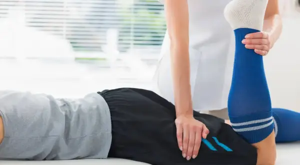 Un physiothérapeute aide un patient à étirer sa jambe pour soulager une crampe cuisse.