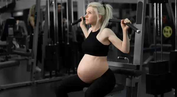 Gravid kvinna tränar rygg med latsdrag. Hon är fokuserad och stark, en inspiration för marklyft gravid.