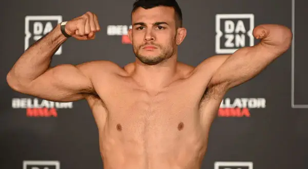 Fighter with one arm boxing, flexing his bicep. He stands against a backdrop of DAZN and Bellator MMA logos.