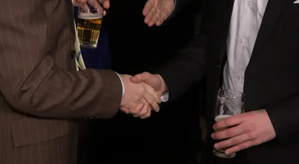 Dwóch mężczyzn w garniturach ściska sobie dłonie, trzymając piwo. Czy to początek udanej transakcji, czy może ukryte wady oświadczenia woli?