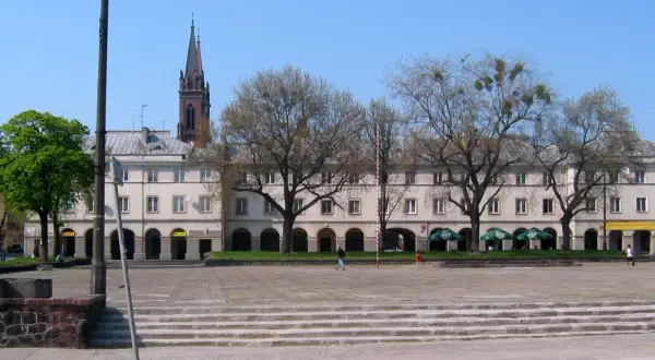 Łódź stare miasto: plac z kamiennymi schodami, arkadowymi budynkami i wieżą kościelną w tle.