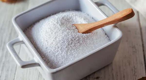 Piatto bianco con percarbonato di sodio e cucchiaio di legno. Informarsi sui percarbonato di sodio controindicazioni prima dell'uso.