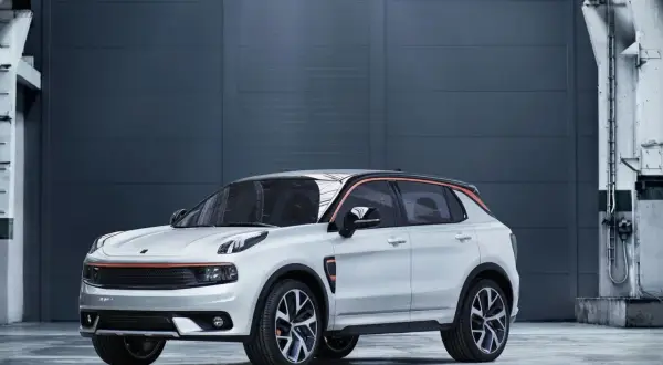 Biały Lynk & Co 01 z pomarańczowymi akcentami stoi przed szarą, industrialną ścianą.