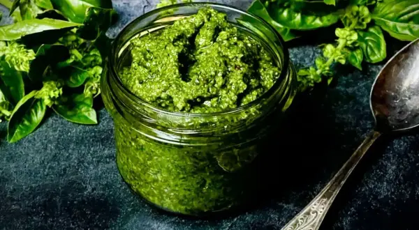 Frisches Basilikum-Pesto in einem Glas, bereit für ein köstliches basilikum pesto rezept. Daneben ein Löffel und grüne Basilikumblätter.
