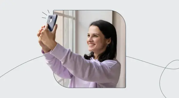 Uśmiechnięta dziewczyna robi selfie telefonem, zastanawiając się, ile zdjęć do dowodu będzie potrzebować.