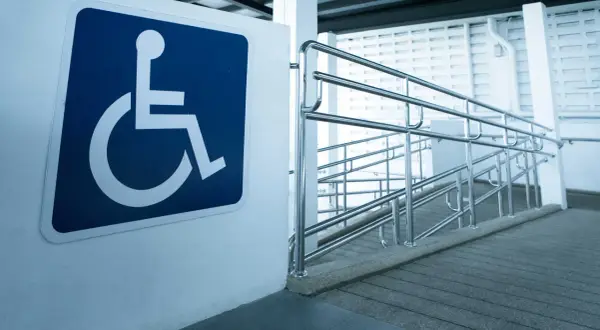 Segnale di accessibilità per disabili accanto a una rampa con corrimano, a norma con la legge 104 per l'abbattimento barriere architettoniche.