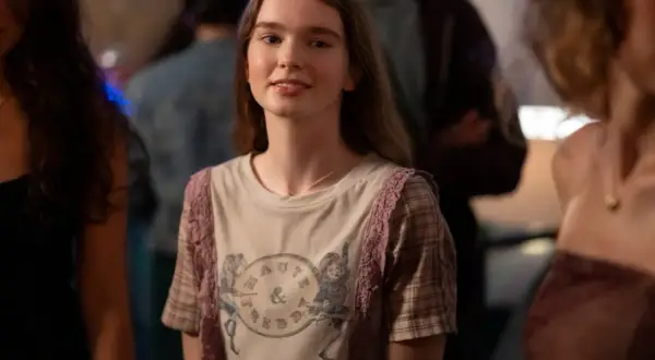 Młoda dziewczyna w koszulce z nadrukiem, przypominająca postać z filmów Chloë Grace Moretz, uśmiecha się na imprezie.
