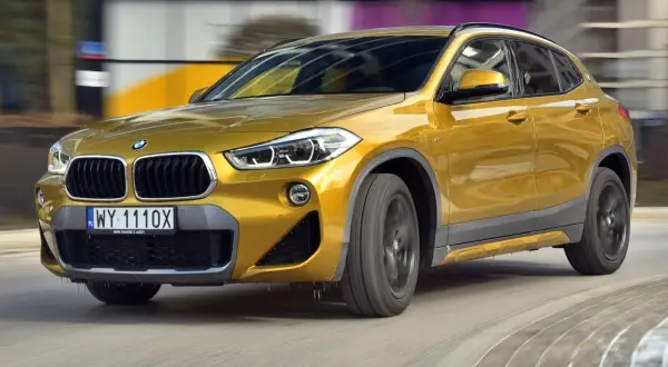 Złoty BMW F39 w ruchu, z widocznym grillem i reflektorami.