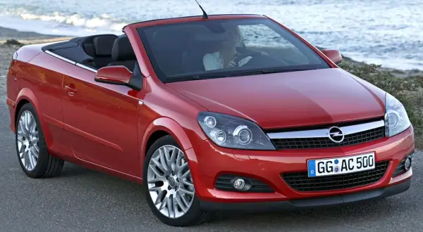 Czerwony opel cabrio z opuszczonym dachem, zaparkowany przy plaży. Kobieta za kierownicą cieszy się jazdą.
