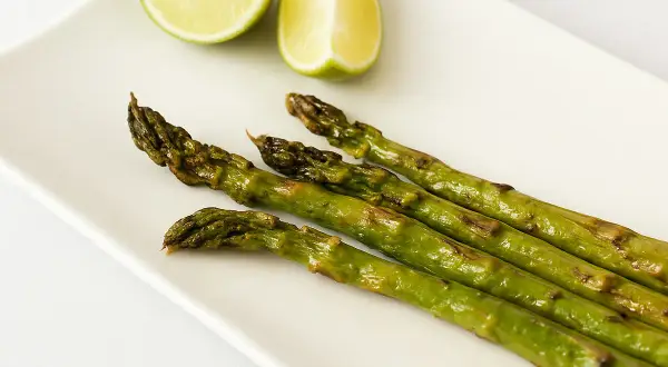 Asperges rôties sur une assiette blanche avec des quartiers de citron vert. Une idée simple pour une recette d'asperges savoureuse.