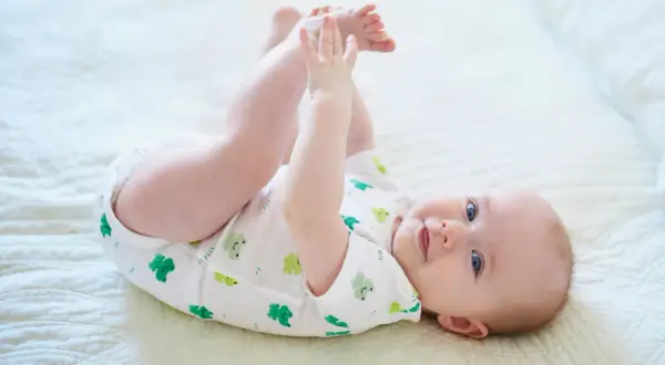 Ein Baby mit 6 Monaten kann schon viel! Dieses Baby liegt auf dem Rücken, hebt seine Beine und spielt mit seinen Füßen.
