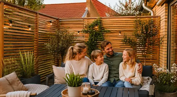 Familj njuter av kvällen på altanen, omgiven av ett vackert insynsskydd i trä.
