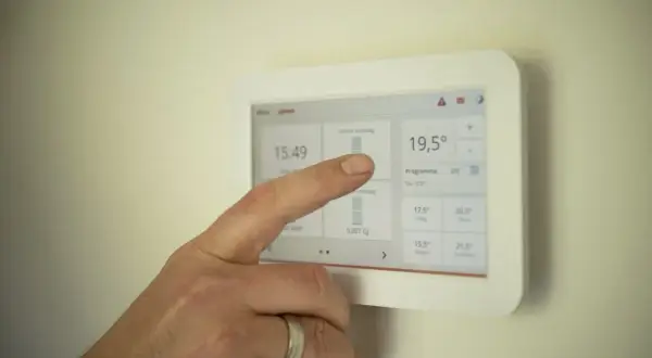 Dłoń dotyka ekranu termostatu, pokazując jak ustawić piec gazowy kondensacyjny ekonomicznie. Widoczna temperatura 19,5°C.