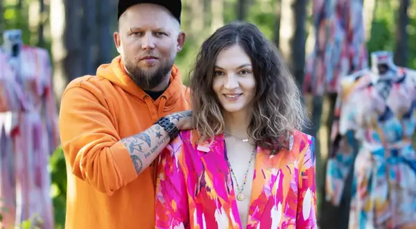 Para pozuje wśród kolorowych sukienek. Mężczyzna w pomarańczowej bluzie, kobieta w marynarce. Naoko - co to za firma?
