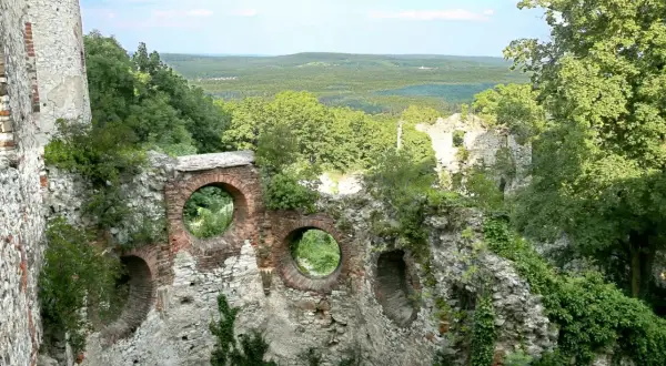 Ruiny zamku Tenczynek z okrągłymi oknami w ceglanym murze, otoczone zielenią i rozległym krajobrazem.