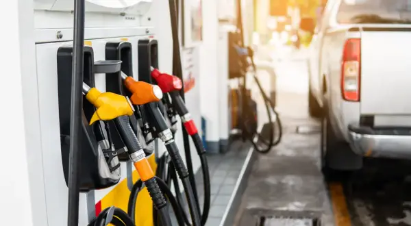 Zapfsäulen mit bunten Zapfpistolen und einem Teil eines Autos an einer Tankstelle.