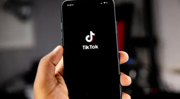 Dłoń trzyma smartfon z logo TikToka. Kiedy powstał TikTok? Aplikacja zadebiutowała w 2016 roku.