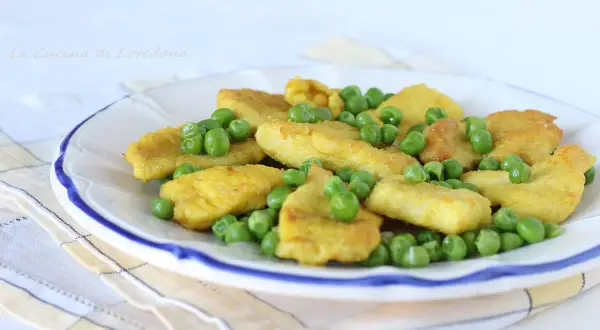 Petto di pollo impanato e dorato, servito con piselli freschi su un piatto bianco bordato di blu.
