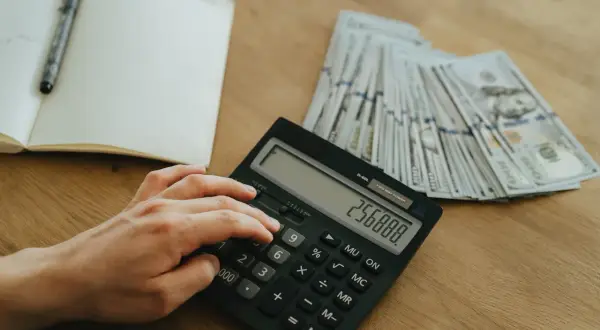 Ręka wpisuje kwotę na kalkulatorze obok stosu banknotów. Planowanie finansowe, jak zatrzymać odsetki u komornika, wymaga precyzji.