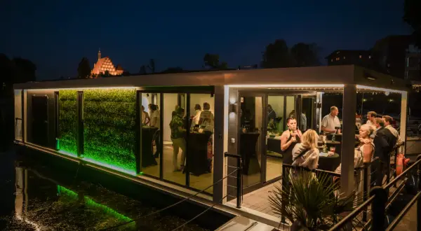 Nowoczesna restauracja na wodzie w Bydgoszczy, z zieloną ścianą i ludźmi bawiącymi się wieczorem. Czy to najlepsza restauracja w Bydgoszczy?