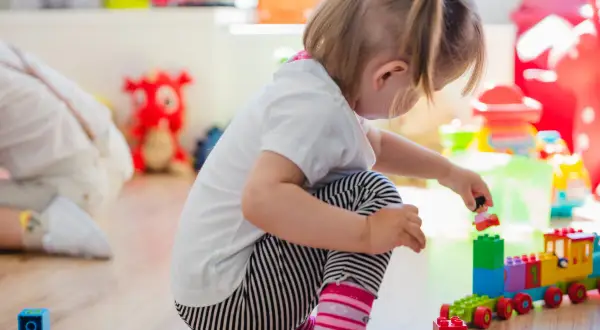 Niña de 0-3 años jugando con bloques de construcción. Crea un tren de juguete y una figura humana.