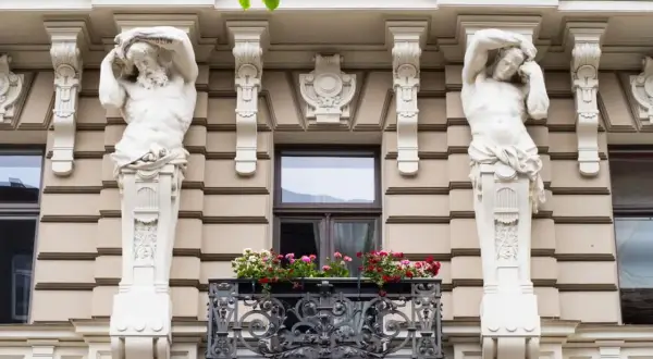 Dwie rzeźby atlantesów podtrzymują balkon z kwiatami. To przykład stylu secesja, co to za sztuka!