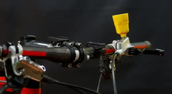 Żółty lejek do odpowietrzania układu hamulcowego zamontowany na kierownicy roweru.