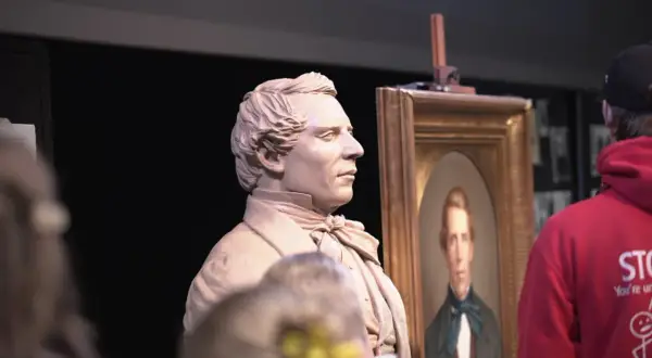 A clay bust of a man stands next to his portrait, perhaps a tribute to who is the most famous sculptor.