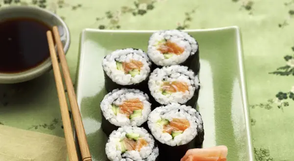 Siedem kawałków sushi z łososiem i ogórkiem na zielonym talerzu. Zastanawiasz się, ile kalorii ma sushi z łososiem?
