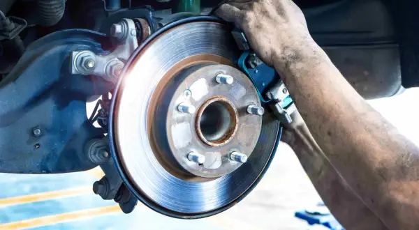 Mécanicien remplaçant la garniture de frein usure d'une Mercedes. Le disque de frein est visible, ainsi que les mains sales du technicien.