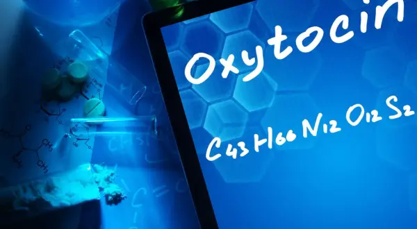Badania nad oksytocyną u mężczyzn. Na ekranie tabletu widnieje nazwa "Oxytocin" i jej wzór chemiczny. Wokół leżą tabletki, proszek i probówki.