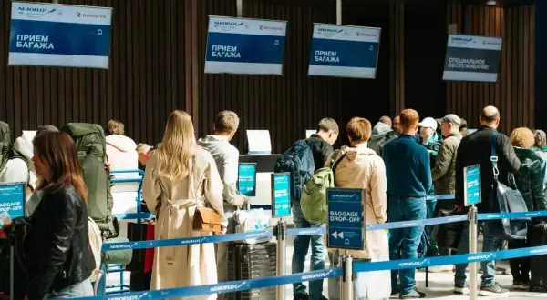 Kolejka do odprawy bagażowej. Na ekranach widnieje napis "BAGGAGE DROP-OFF", ale nie ma żadnego "no show".
