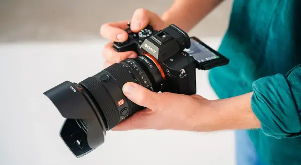 Dłonie trzymają aparat Sony a7r5 z obiektywem.