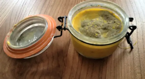 Terrine le parfait recette : un pot en verre avec un couvercle orange ouvert, contenant une préparation jaune et verte sur une table en bois.