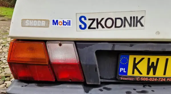 Tył białego samochodu Skoda z naklejkami "Mobil" i "Szkodnik". Widoczna tablica rejestracyjna KWI.