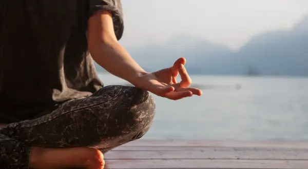 Persona meditando en posición de loto, con la mano en mudra Gyan, susurrando el mantra om.