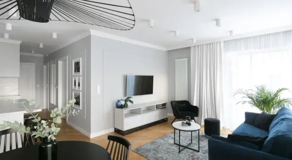 Nowoczesna aranżacja mieszkania w bloku 60 m. Salon z granatową kanapą, czarnym fotelem i stolikami. W tle kuchnia i jadalnia.