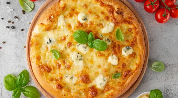 Une délicieuse pizza 4 fromages, dorée et garnie de basilic frais, prête à être dégustée.