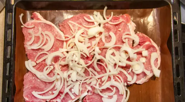 Plastry schabu pieczonego w cebulce, przyprawione i ułożone na blasze wyłożonej papierem do pieczenia.