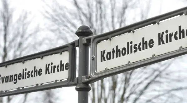 Straßenschilder zeigen "Evangelische Kirche" und "Katholische Kirche". Ein deutlicher Unterschied katholisch evangelisch, der die Vielfalt der Glaubensrichtungen symbolisiert.