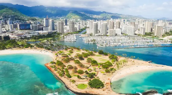 Widok na Honolulu, stolicę Hawajów, z plażą, parkiem i mariną pełną jachtów. W tle góry i drapacze chmur.