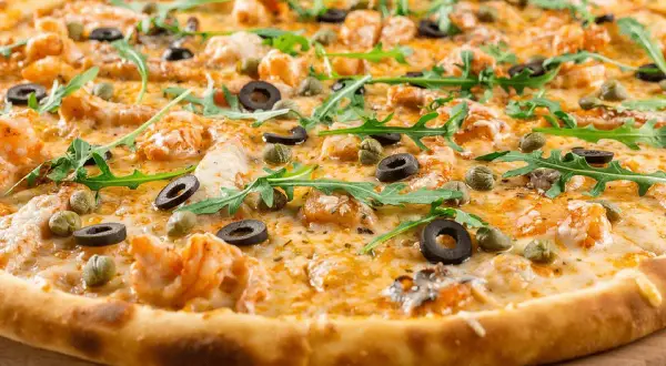 Pyszne ciasto na pizzę z krewetkami, oliwkami, kaparami i rukolą.